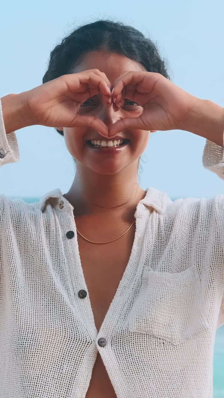 Woman making a heart shape with hands at the beach during sunset