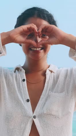 woman making a heart shape with hands at the beach during sunset