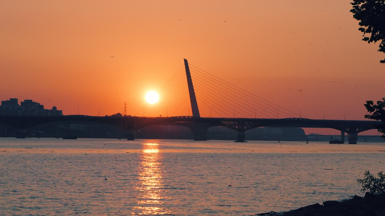 Peaceful static shot of a beautiful golden sunset over the Han River in Seoul, with the sun reflecting on the water and the iconic Seongsan Bridge silhouetted in the distance from Hangang Park