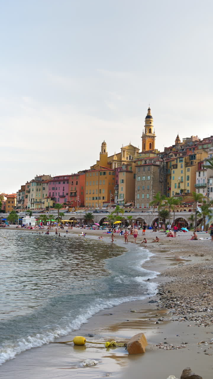 Persone che nuotano nel mare con vista sugli edifici colorati di Mentone, Francia. Verticale