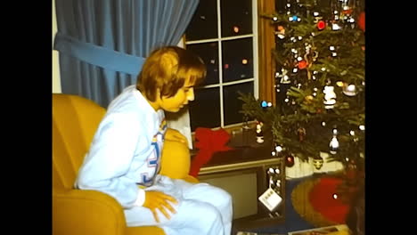 woman and child sitting near christmas tree in 1970s usa. circa usa - 1970s: a woman sits next to a child near a christmas tree, captured in a 1970s video from the united states.