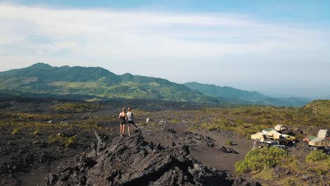 Drone-Aéreo-Volando-Sobre-Dos-Niñas-De-Pie-Sobre-Una-Roca,-Observando-El-Hermoso-Paisaje-Después-De-Una-Caminata,-Viaje-De-Campamento-En-Guatemala