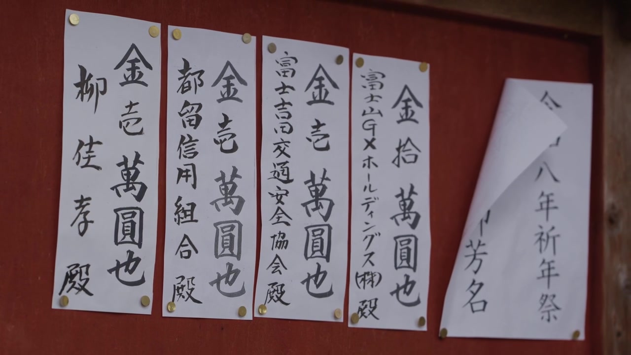 Feuilles de vœux blanches ornées de calligraphie japonaise, épinglées sur un mur rouge de sanctuaire shinto au Japon