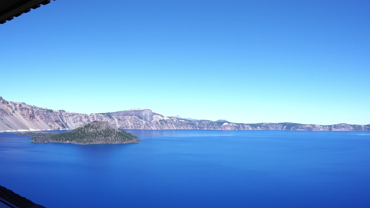 A stunning view of Crater Lake in Oregon featuring deep blue water, Wizard Island, and clear summer skies surrounded by rugged caldera cliffs