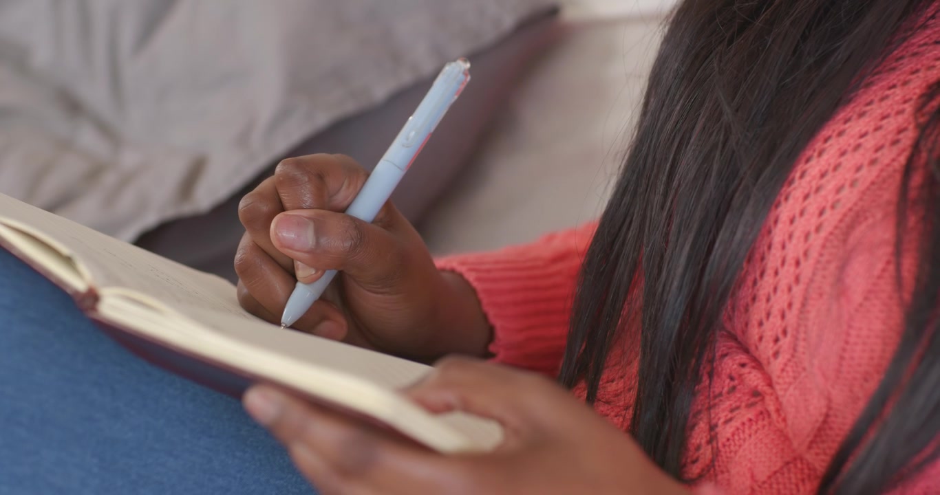Right hand is lowering blue pen, pen tip touching notebook and writing notes on lap