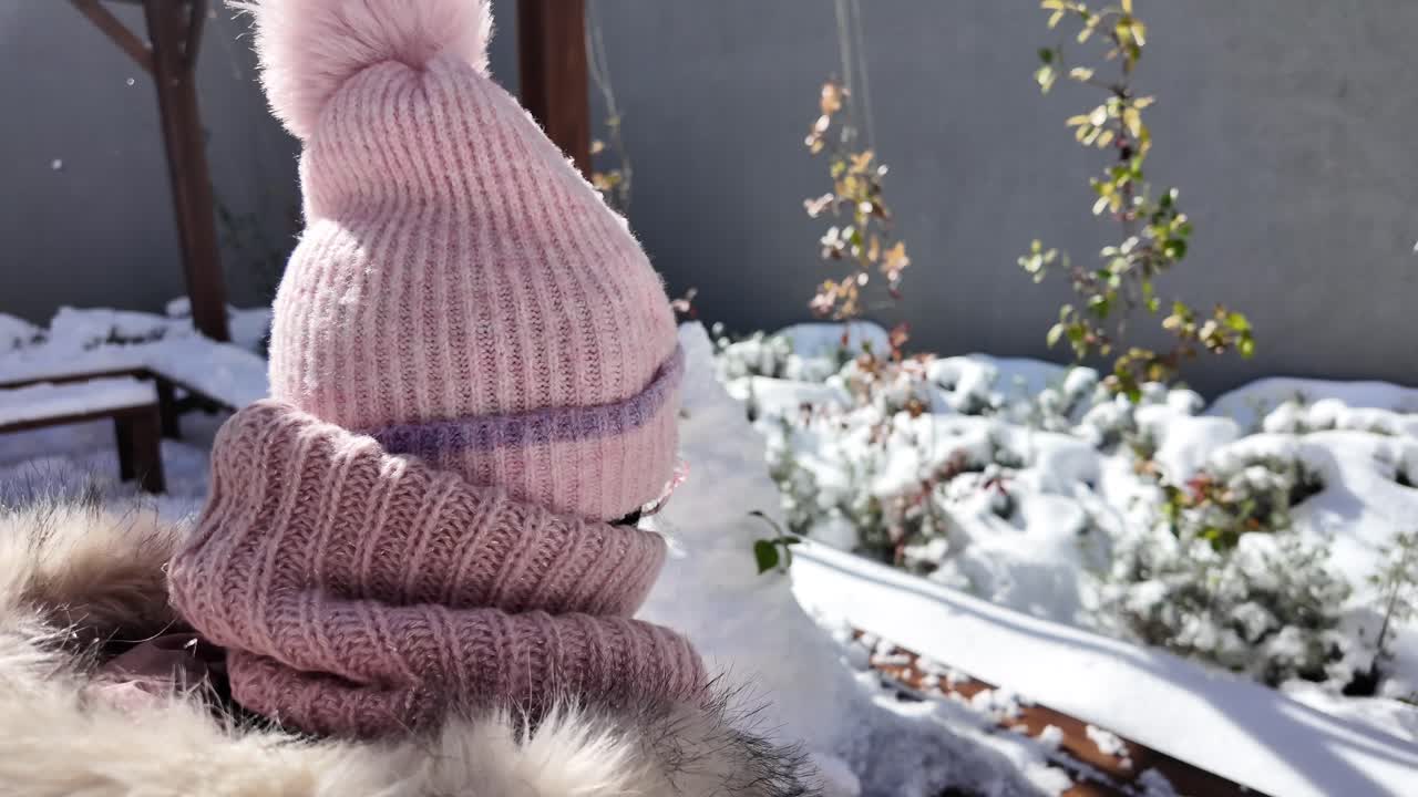 눈 인 정원에서 분홍색 모자와 스카프를 입은 여자