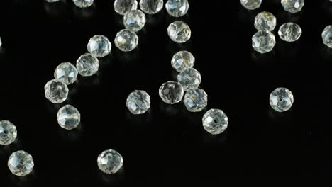 cuentas blancas para hacer joyas en una superficie negra y giratorias. 4k video de primer plano de piedras iridescentes para joyas.