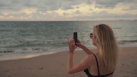 a young attractive woman in swimsuit takes a photo with her cell phone on the beach