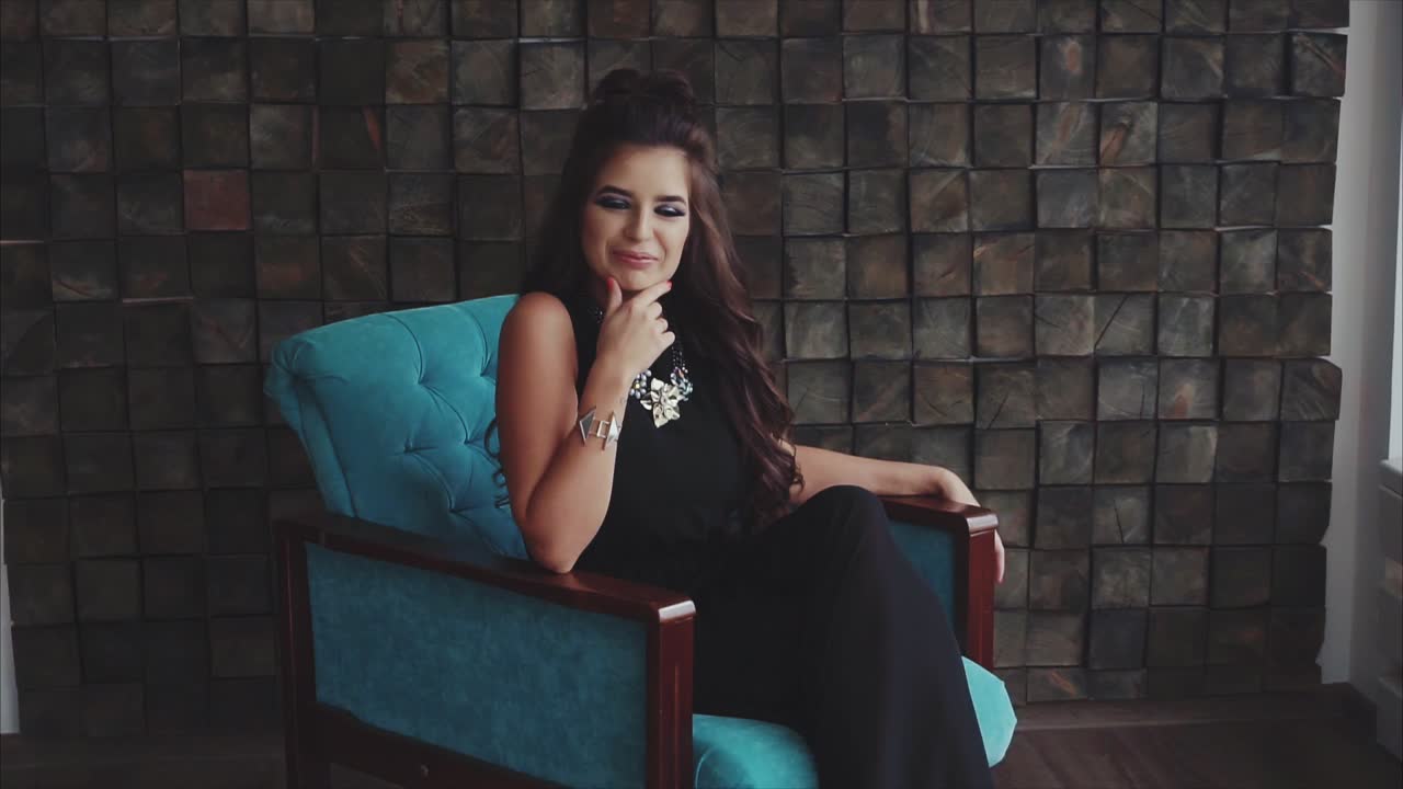 mujer en un vestido negro sentada en una silla turquesa