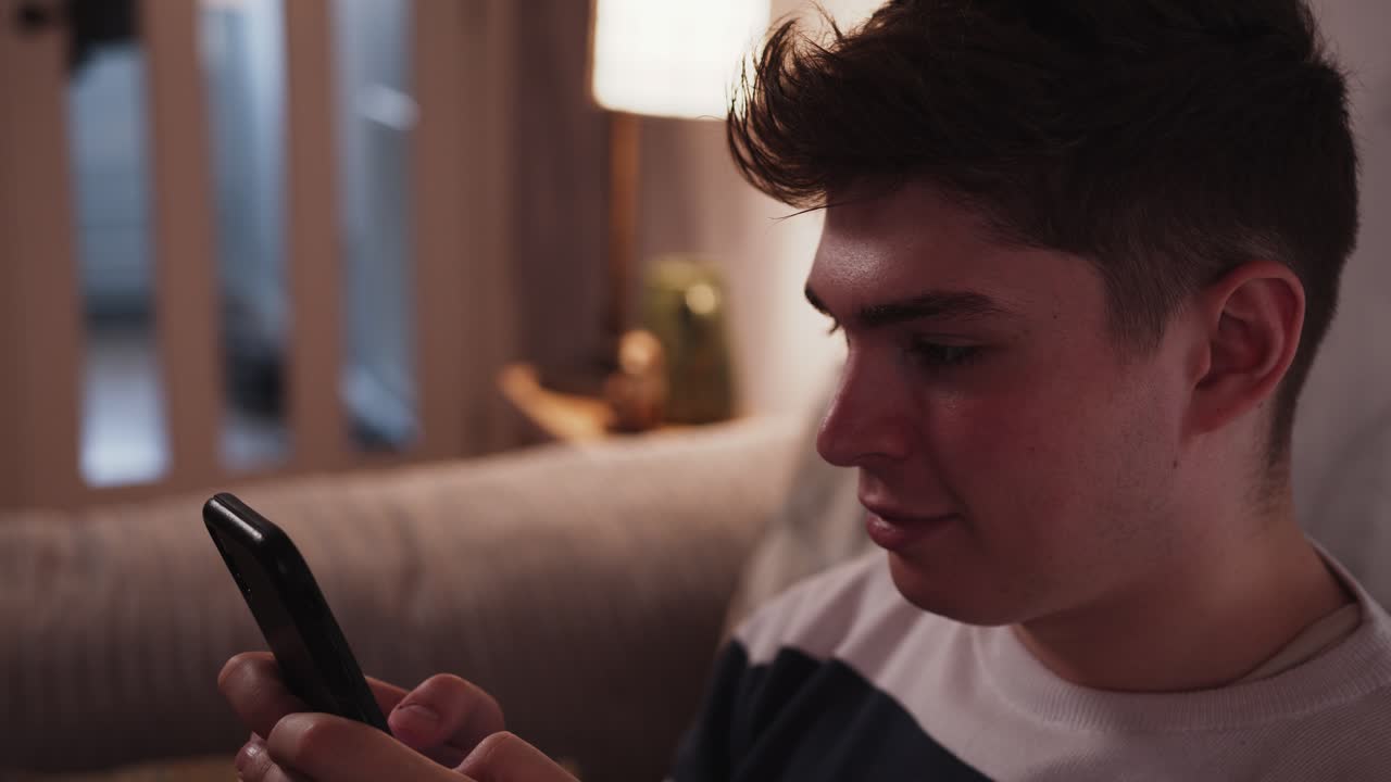 소파 에 집 에 앉아서 스마트폰 으로 문자 메시지 를 보내는 동안 미소 짓는 젊은 남자