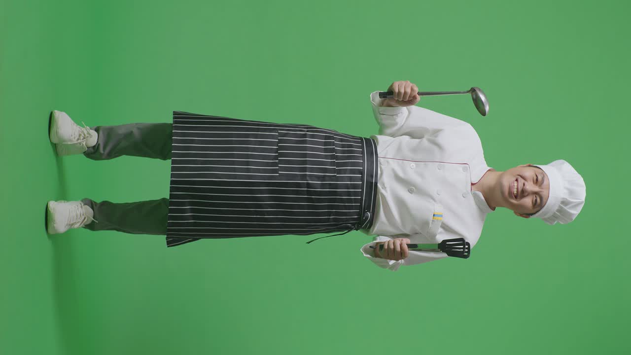 Full Body Of Asian Man Chef Smiling And Showing Tongs And Ladle To Camera While Standing In The Green Screen Background Studio