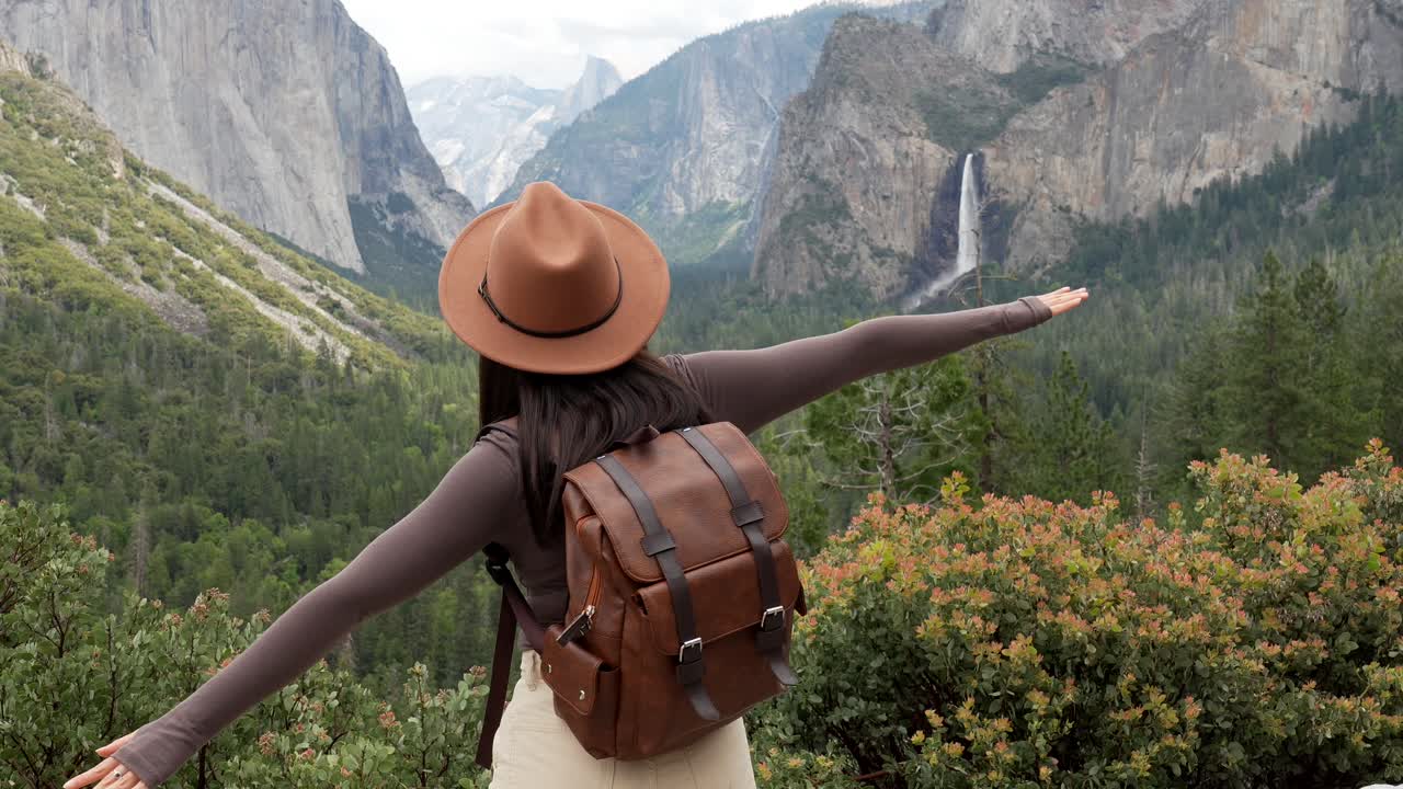 Donna felice con zaino e cappello che si gode la vista di una cascata di montagna