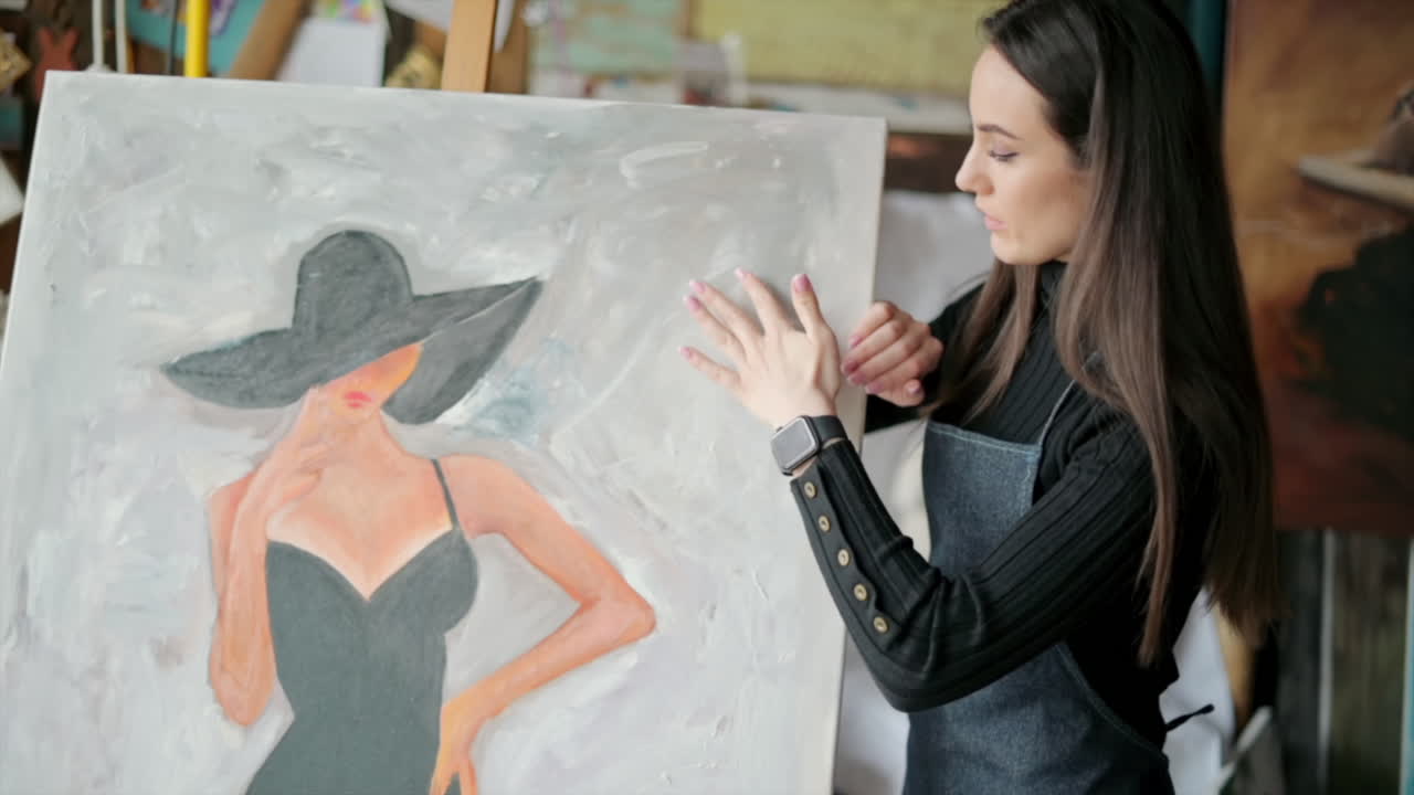 Woman painter wearing black clothes painting woman model face with hat drawing with red brush at a workshop