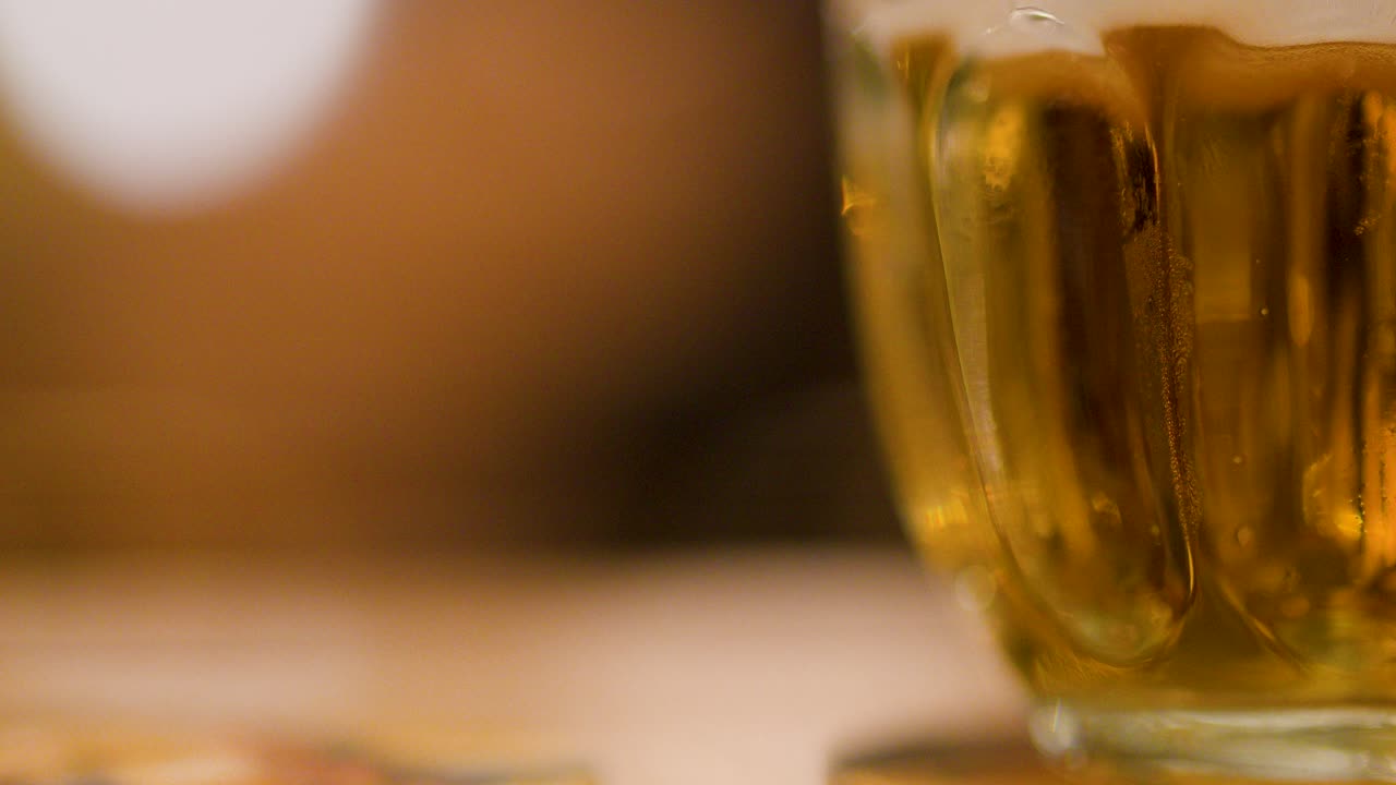 Closeup of lager beer with foam in glass mug at a brewpub, warm ambient setting