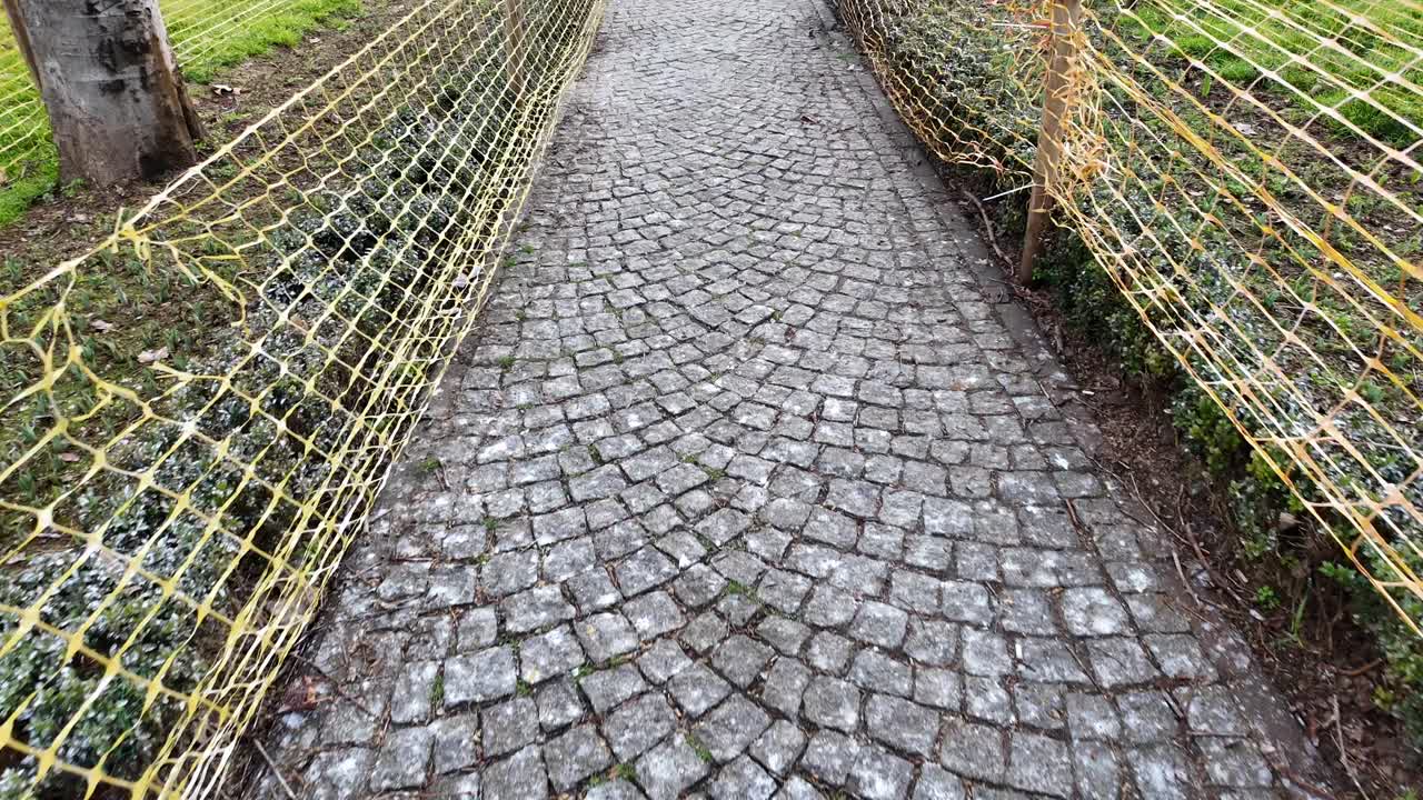 Walking Along a Cobblestone Path Lined with Yellow Fences