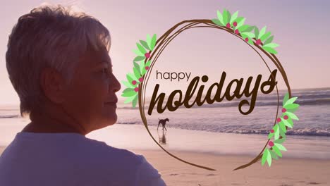 Animation-of-happy-holidays-over-biracial-senior-woman-on-beach