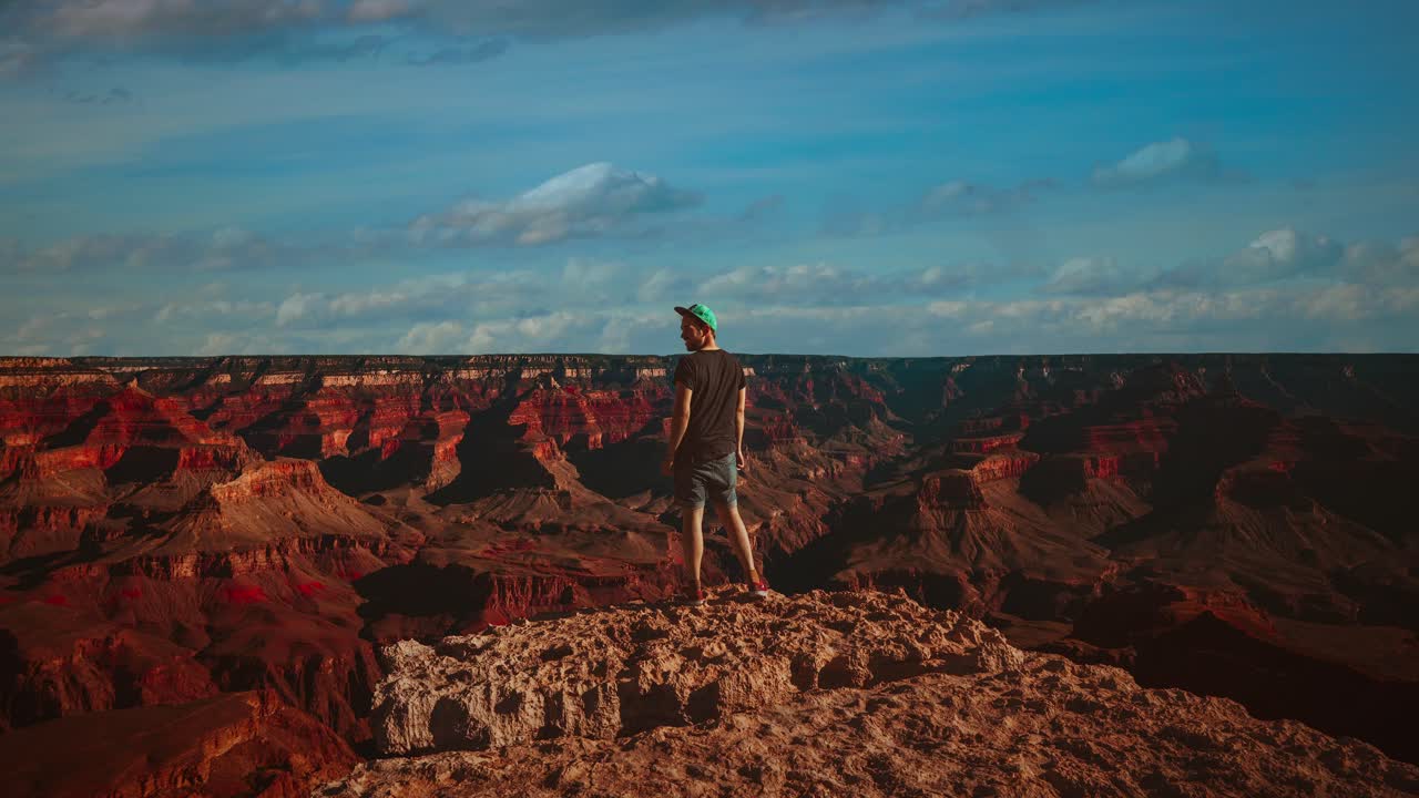 cinemagraph - lapso de tiempo de bucle de video sin interrupciones de un joven que mira por encima del vacío profundo y las formaciones rocosas en el famoso gran cañón en arizona, américa - ee.uu. con nubes que cruzan el cielo azul
