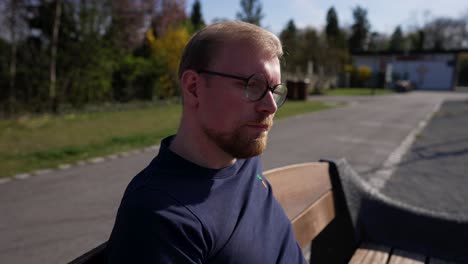 Handsome-Man-Smokes-a-Casual-Cigarette,-Sitting-on-Bench-on-Sunny-Day,