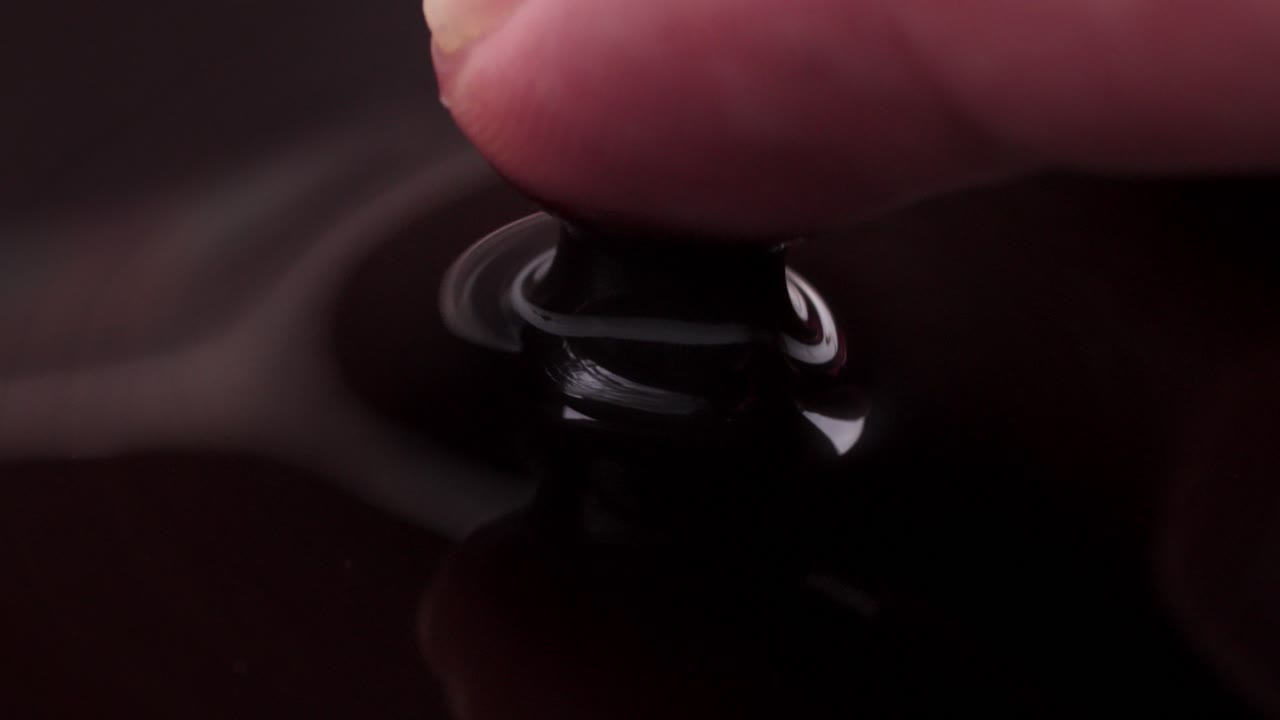 A finger pressing into black liquid, creating ripples and showing swirling movements