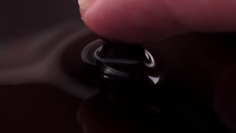 a finger pressing into black liquid, creating ripples and showing swirling movements