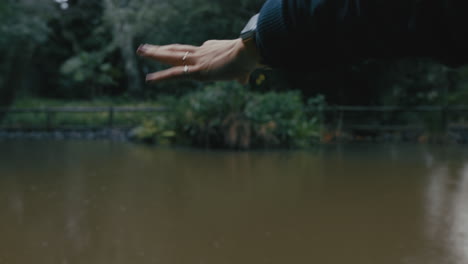 Nahaufnahme-Einer-Frau,-Die-Mit-Der-Hand-Regen-In-Einem-Wunderschönen-Gartenpark-Mit-Teich-Fängt-Und-An-Einem-Kalten-Wintertag-Sanften-Nieselregen-Genießt