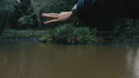 close up woman hand catching rain in beautiful garden park with pond enjoying gentle drizzle on cold winter day