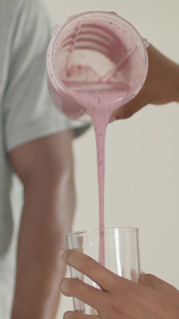 Video verticale: Alzando la tazza, persona che inclina e versa un frullato rosa in un bicchiere in cucina, maglietta