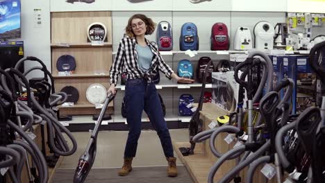 Funny-caucasian-woman-in-casual-standing-in-home-appliance-store---dancing,-having-fun-with-handheld-vacuum-cleaner,-funky