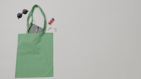 green bag with sunglasses, notebook, lipstick on white background, copy space, slow motion