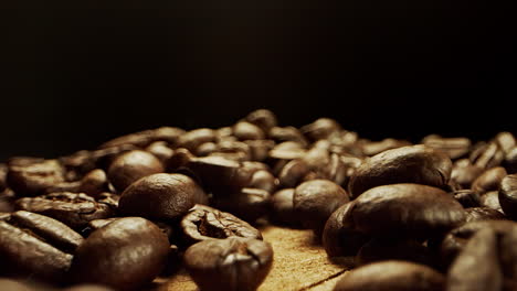 close camera movement through falling fresh coffee beans into a pile of beans laying on a wooden surface