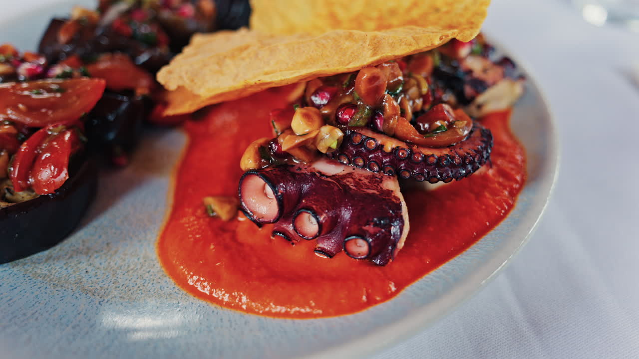 Close up of grilled octopus on a plate, garnished with a rich red sauce