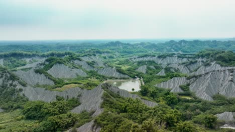 Aerial-flight-over-mud-volcanic-area-with-lake-and-landscape-riding-cloudy-day-in-Taiwan