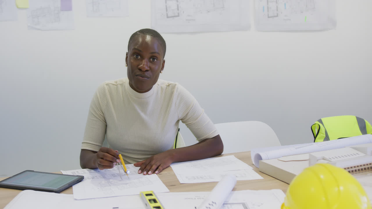 Portrait of happy african american female architect sitting at desk with blueprints