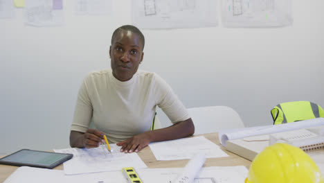 retrato de una feliz arquitecta afroamericana sentada en un escritorio con planos
