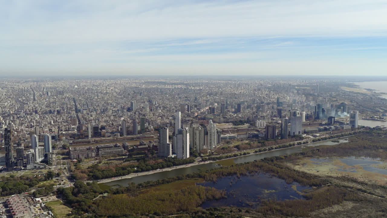Wide aerial view of Buenos Aires city skyline with urban buildings, green areas and the Rio de la Plata river in the background
