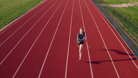 teen girl athlete sprints on a high school track aerial camera preceding