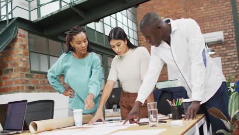 happy diverse architects looking at architectural blueprints and discussing work at office