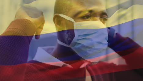 animation of flag of colombia waving over man wearing face mask during covid 19 pandemic