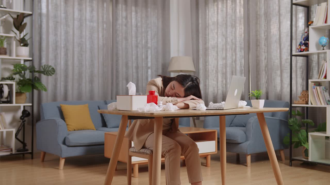 아픈 아시아 사업가 여성이 집에서 거실에서 노트북으로 일하면서 테이블에서 잠을 자고 있습니다.