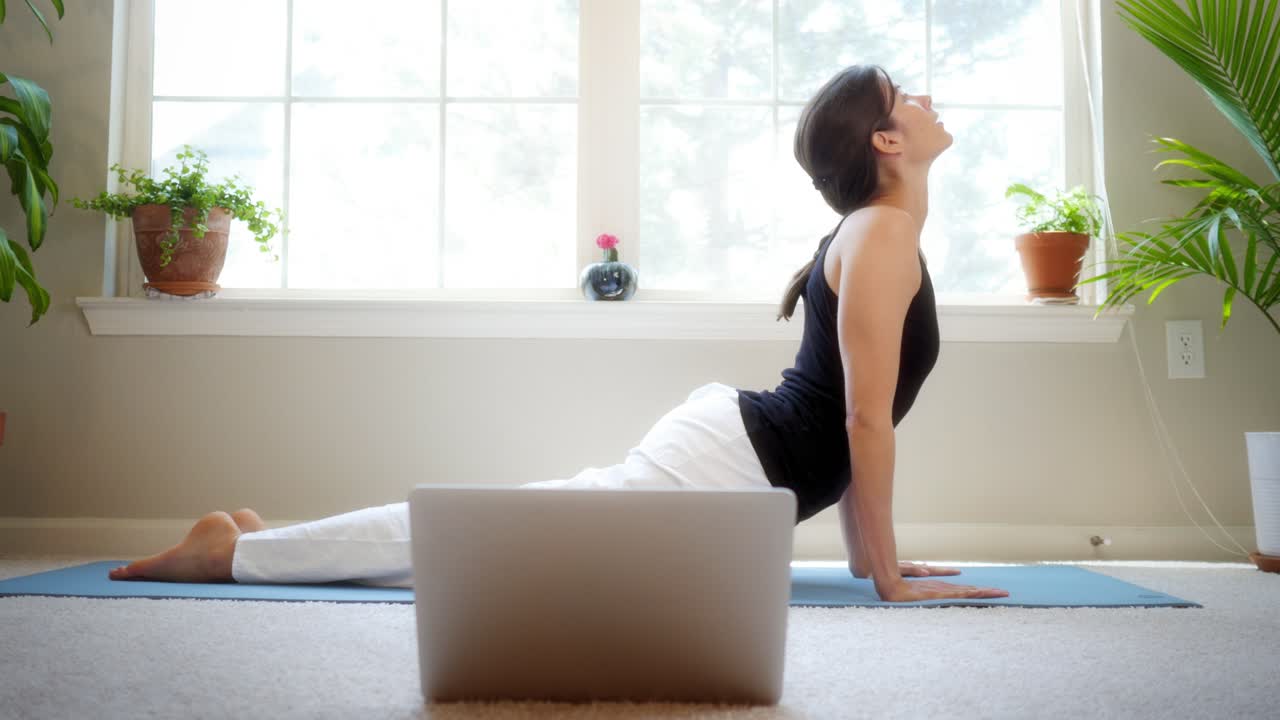 Pretty girl stretches while taking a remote yoga class in her house while quarantined