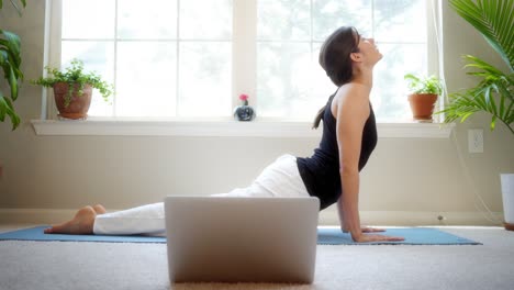 Pretty girl stretches while taking a remote yoga class in her house while quarantined
