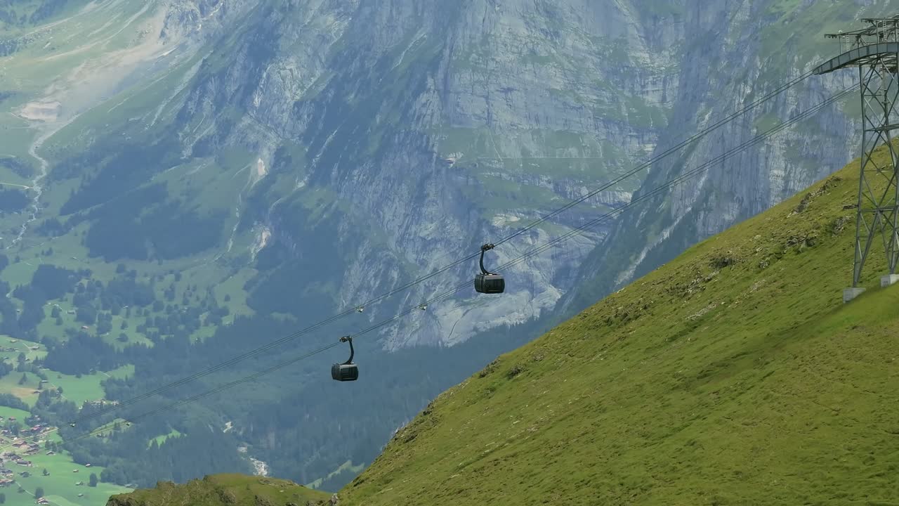 Gondola cable cars moving above the lush green valley of Grindelwald, Switzerland, aerial close up shot