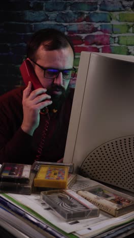vertical view of it guy or programmer talking over landline telephone in front of desktop computer monitor