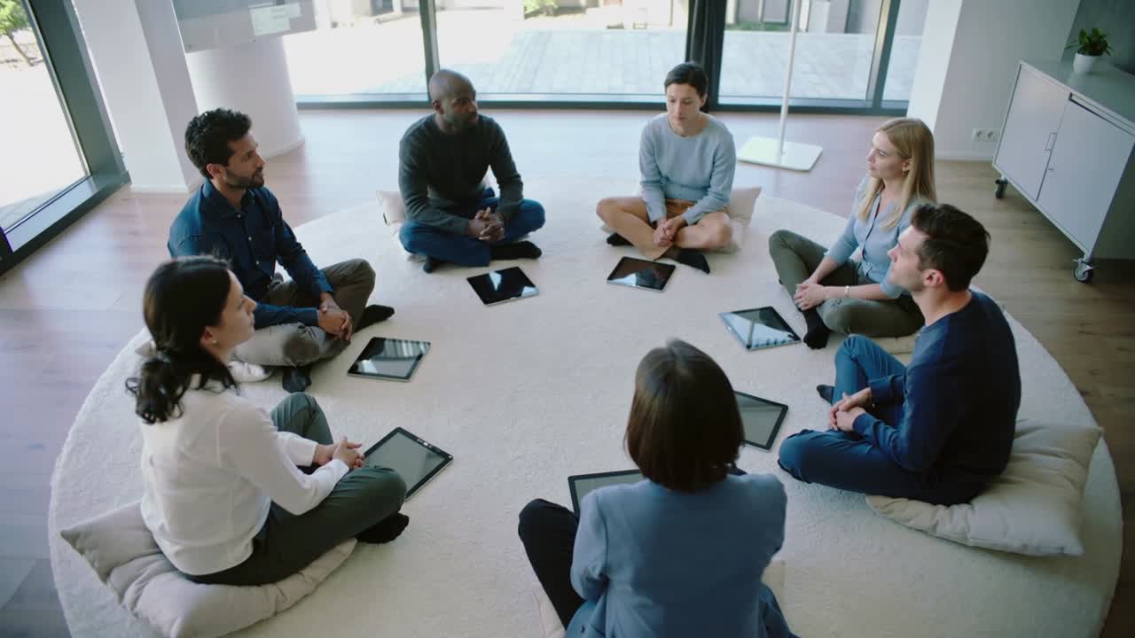 Een facilitator in blazer die een groepsdiscussie leidt in een vergadering met 7 tablets voor planning.