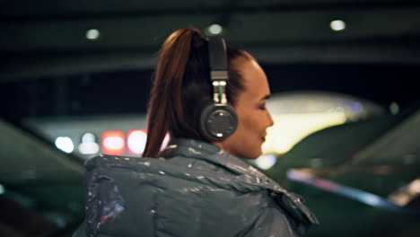 Chica-Brillante-Caminando-En-El-Metro-Con-Auriculares-En-Primer-Plano.-Mujer-Escuchando-Música-Noche-Ciudad