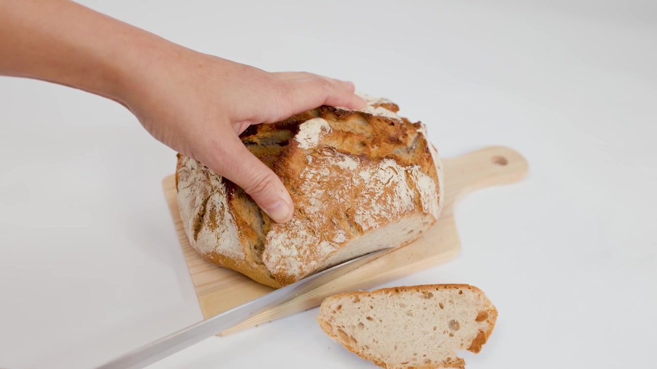 Person Slicing Fresh Crusty Sourdough Bread on Wooden Board