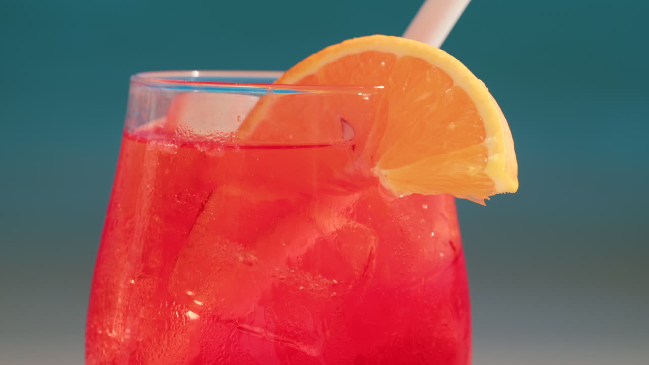 Primo piano di un cocktail rosso-arancio rinfrescante con una fetta d'arancia e cubetti di ghiaccio, scattato all'aperto in una giornata di sole a Cannes