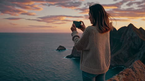 woman capturing a scenic coastal sunset with her phone