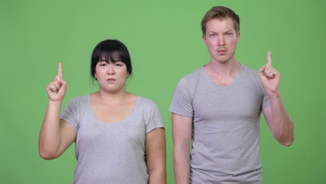 young multi-ethnic couple pointing up together