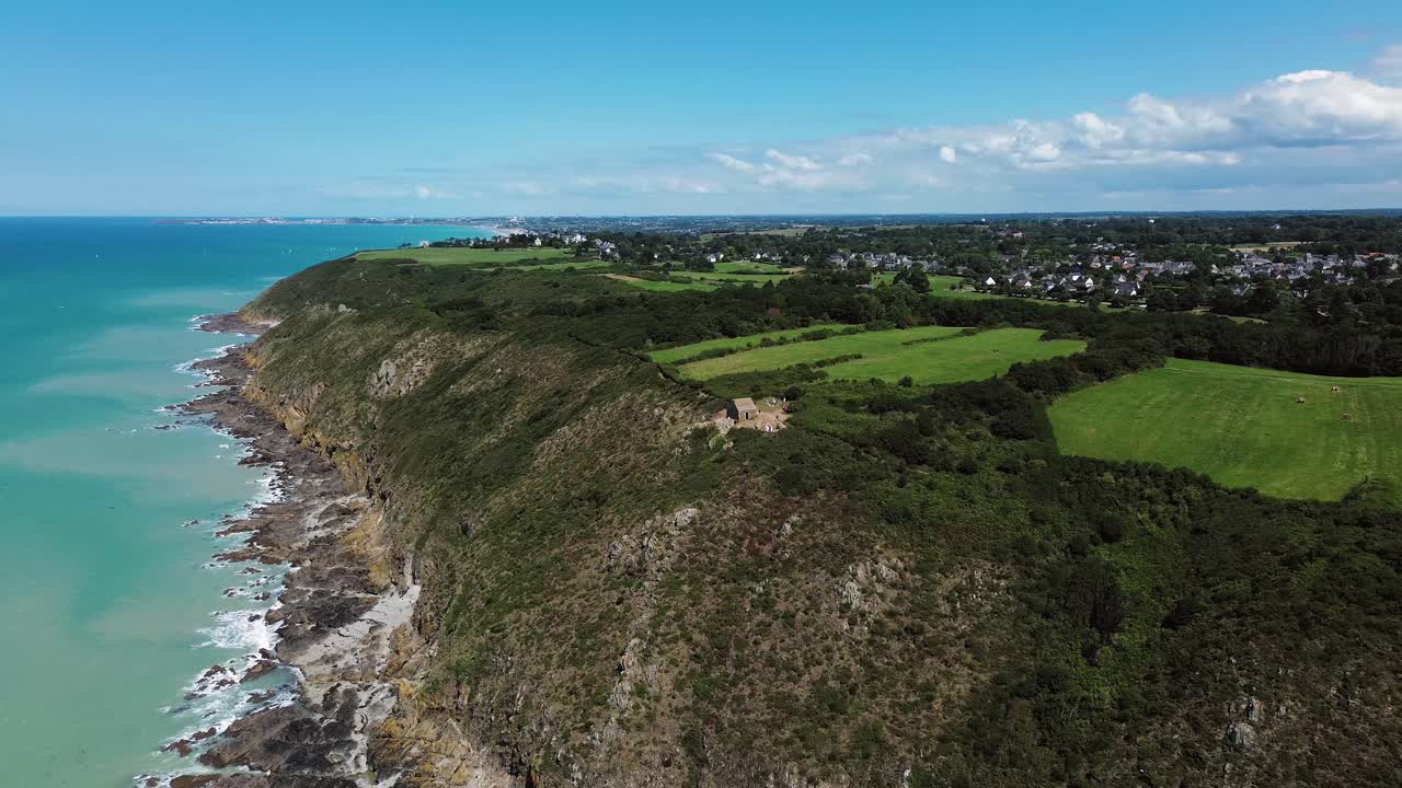 From above, the Cabane Vauban appears nestled atop the wild cliffs of Carolles, surrounded by wind-swept grass and the vast sea below